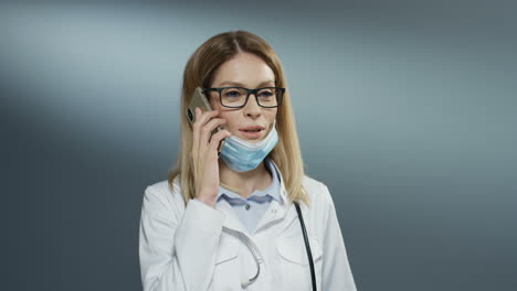 Beautiful-young-Caucasian-woman-doctor-in-glasses-taking-off-mask-from-mouth-and-speaking-cheerfully-on-the-phone-and-smiling.-Close-up.